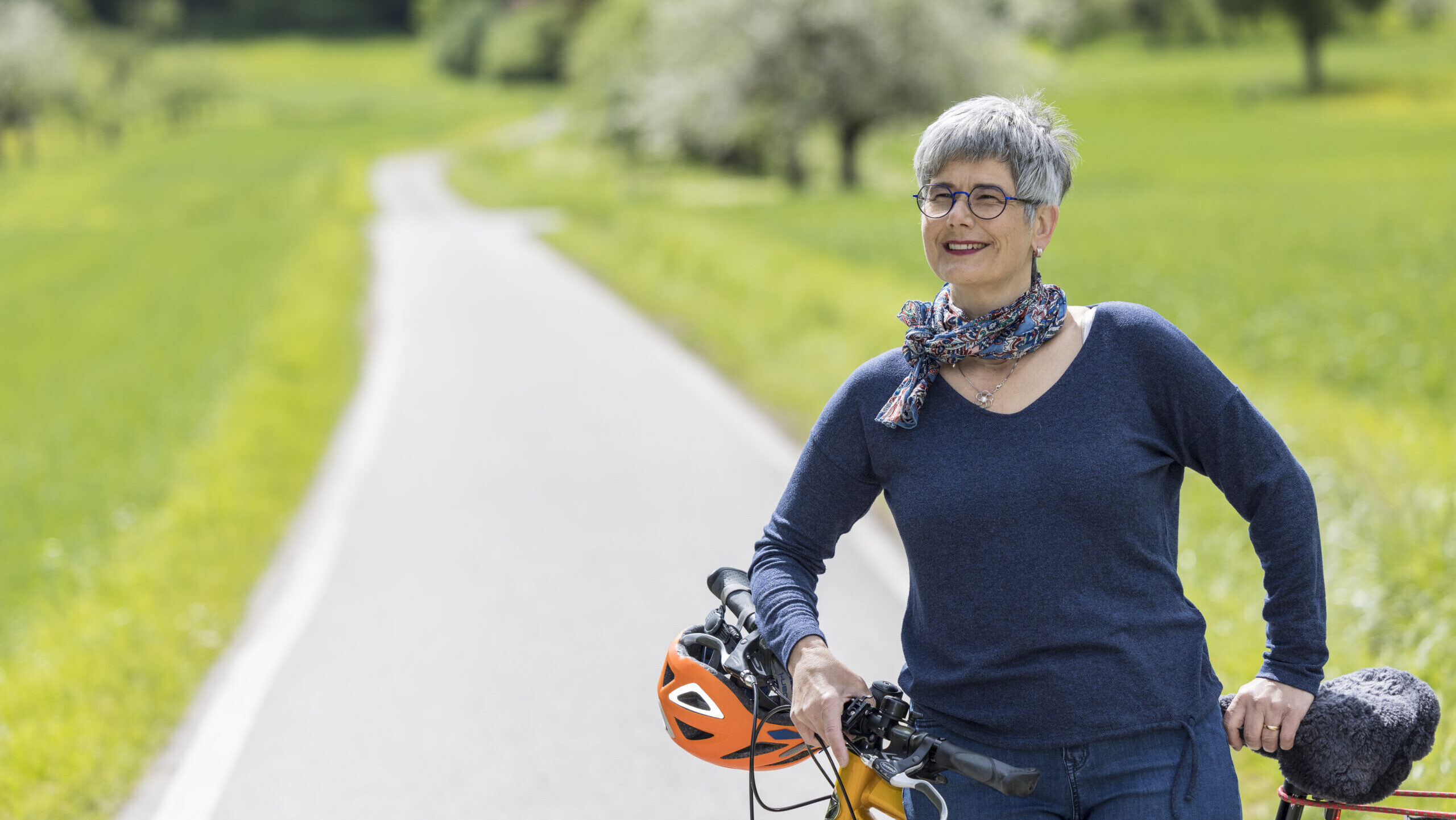 Barbara Feichtinger steht lächelnd mit einem Fahrrad in der Natur